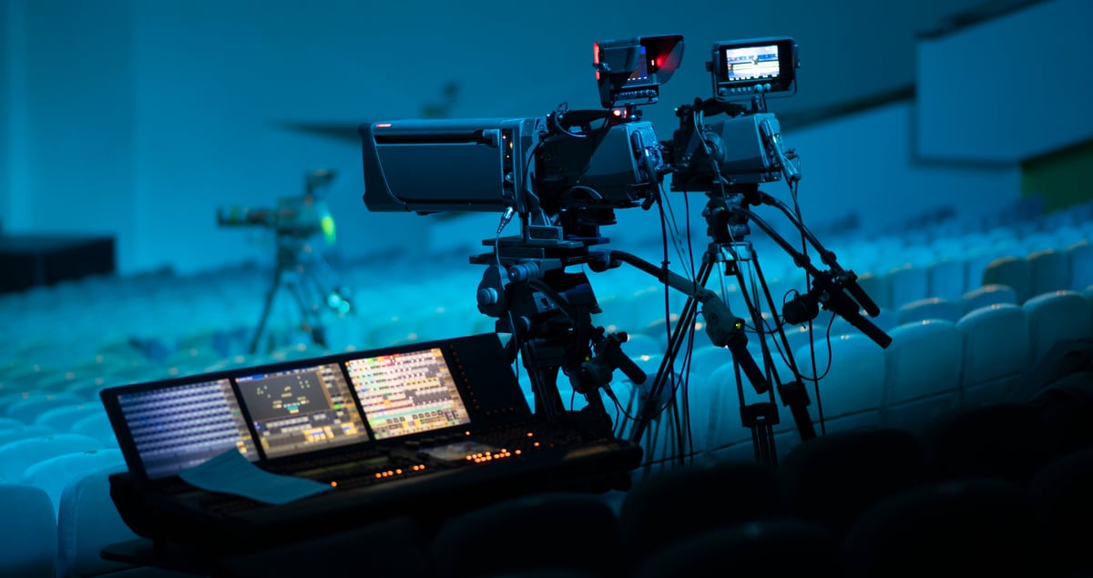 High-end broadcasting equipment with digital video switcher and professional cameras on tripods in a dark auditorium. Cinematic lighting, bokeh background